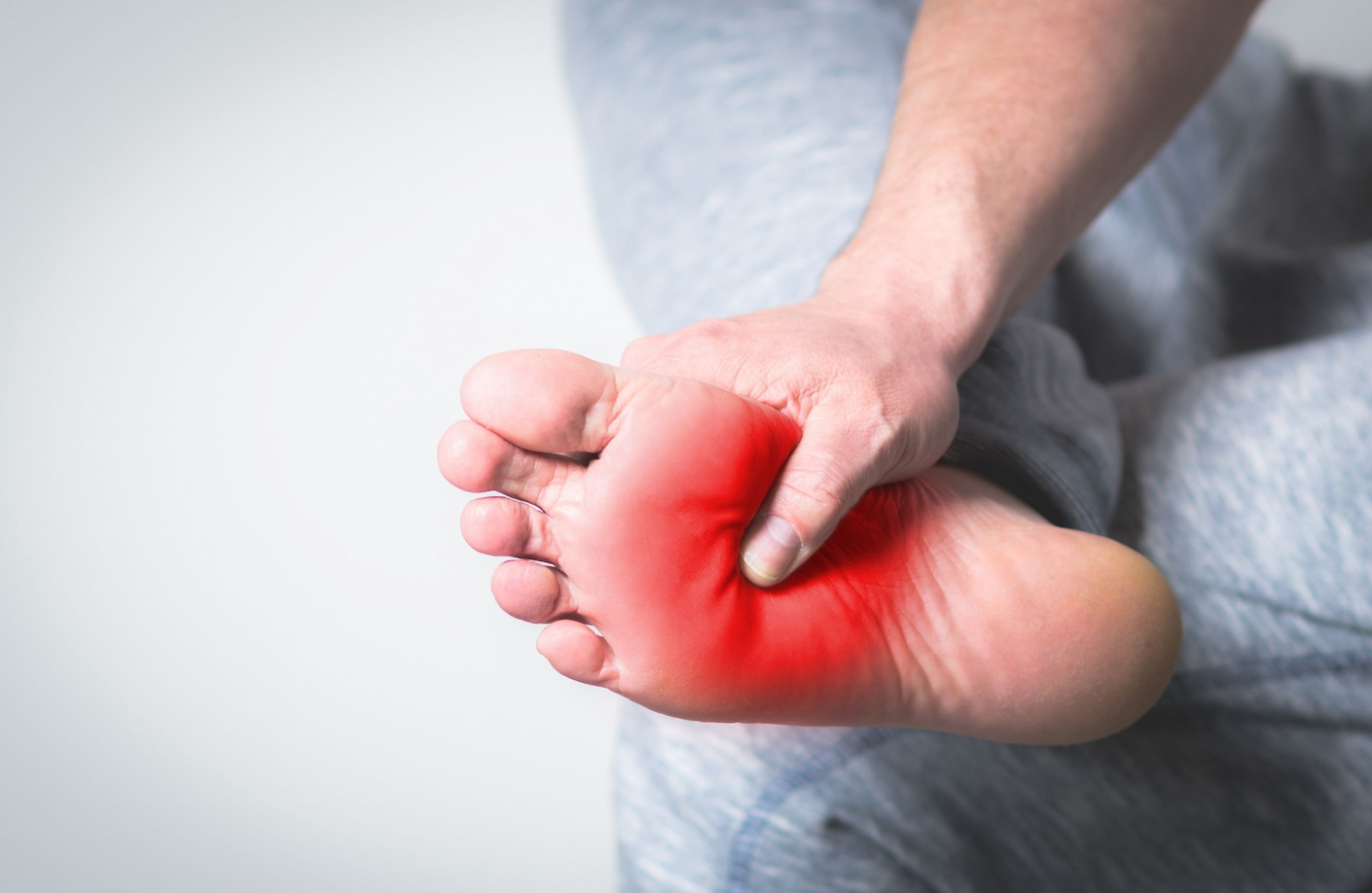 Homme se tenant le pied droit entre ses mains, la jambe droite croisée avec une douleur au niveau de l'arche du pied droit.